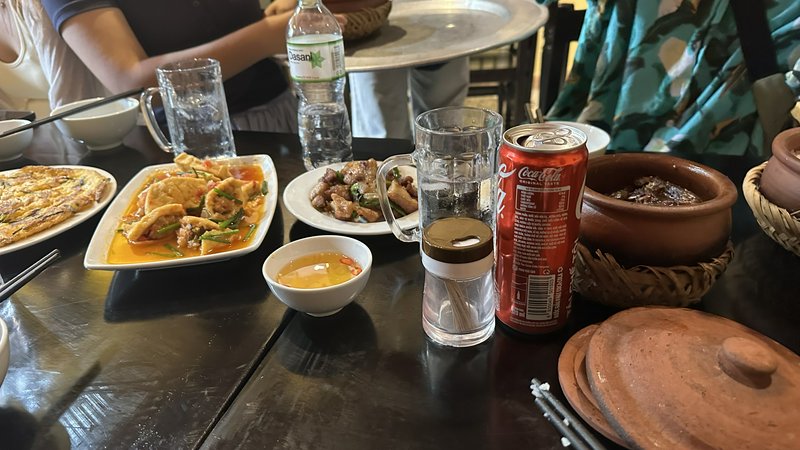 Casual group restaurant spread of Southeast Asian dishes, drinks, and terracotta cookware arrange...