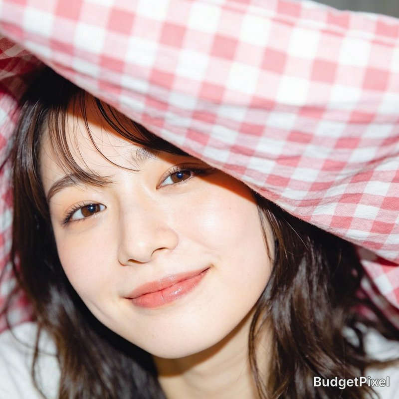 Close-up portrait of a smiling young East Asian woman peeking out from under a pink gingham check...