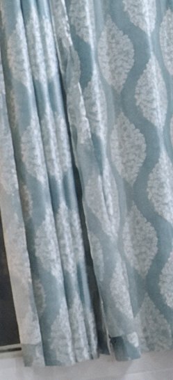 Close-up of pleated dusty blue curtain fabric with raised textured off-white repeating ogee leaf ...