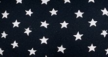 Close-up of soft black fabric printed with evenly scattered, repeating white five-pointed star pa...