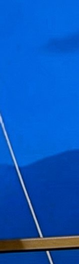 Close-up partial view of a bright blue table tennis surface marked with white lines and a wooden ...