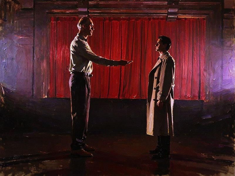 Two men face each other, one extending a hand, on a stage in front of red theater curtains
