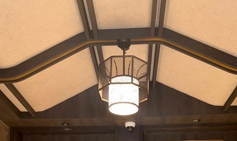 Low angle view of a lit hexagonal metal mesh pendant light mounted on a dark wood coffered vaulte...