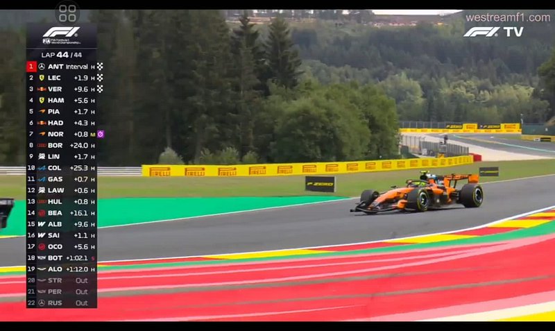 Orange McLaren Formula 1 car races on a forested race track, with F1 live standings overlay for t...