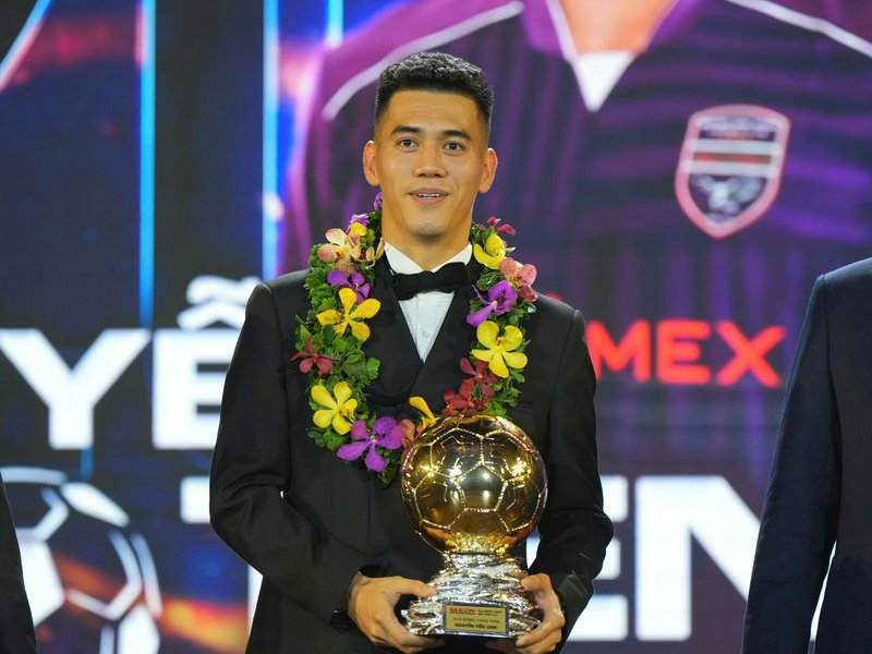 Vietnamese professional footballer holds a golden soccer trophy, wearing an orchid lei and tuxedo...