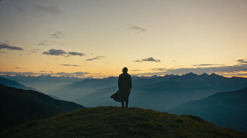 Person stands on a hilltop overlooking a misty mountain range at sunset