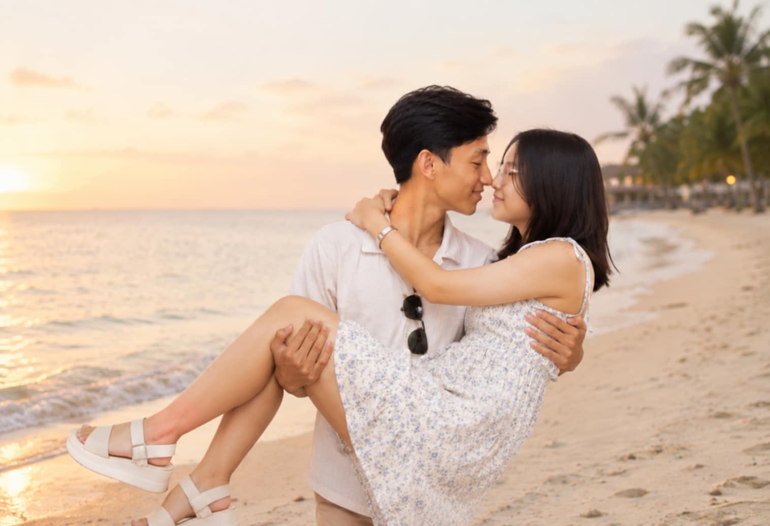 Young man tenderly carries his partner as they share an intimate moment on a tropical beach at golden sunset.
