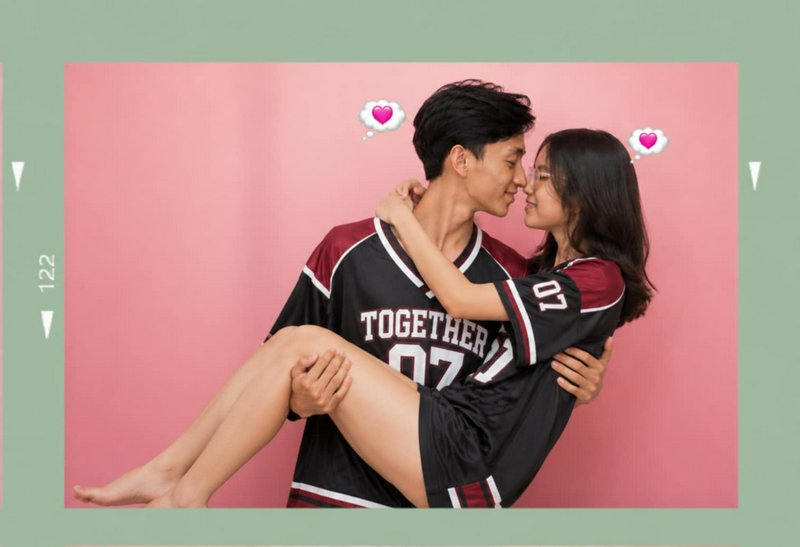 Young man carrying his partner in matching couple jerseys, with heart thought bubbles, pastel pin...