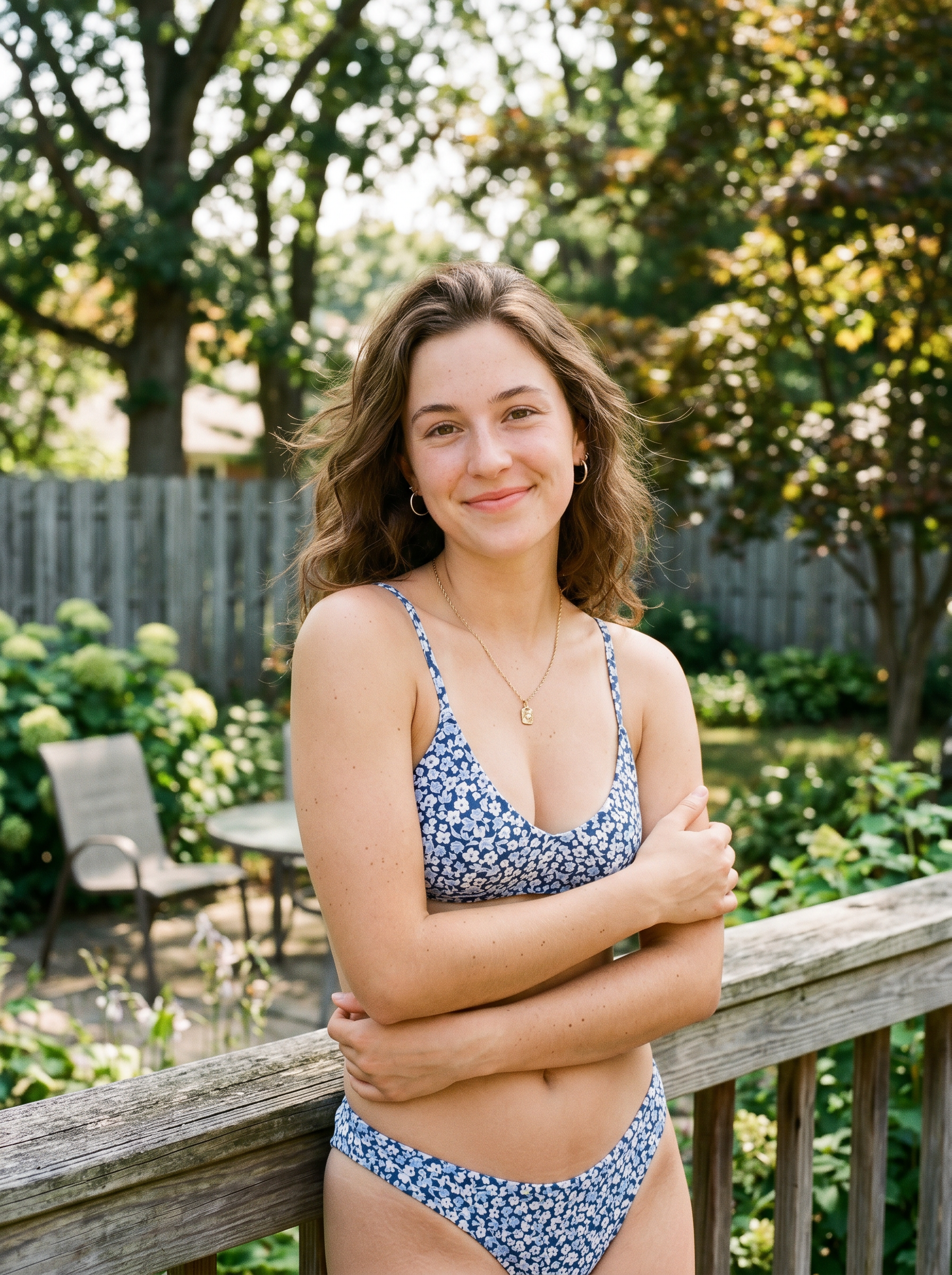 Woman in blue floral bikini standing on a wooden deck in a sunny garden outdoor setting.