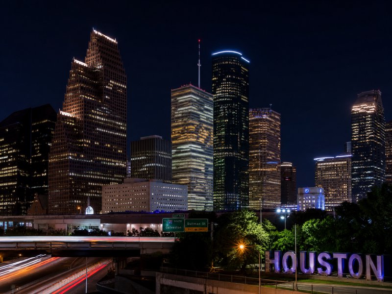 Night view of Houston skyline with illuminated skyscrapers and freeway signals.
