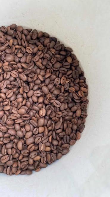 Top-down view of a dense pile of medium roasted brown coffee beans resting on a pale off-white textured surface.