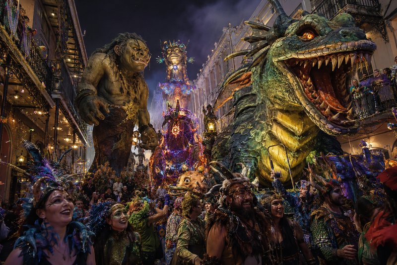 Night parade with a giant dragon float and mythical creatures among colorful costumes on a crowded street.