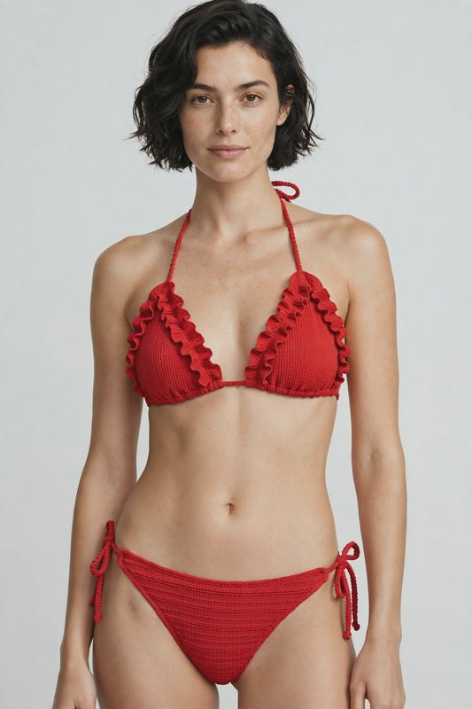 Model wearing a ruffled textured red triangle bikini against a plain light gray studio background