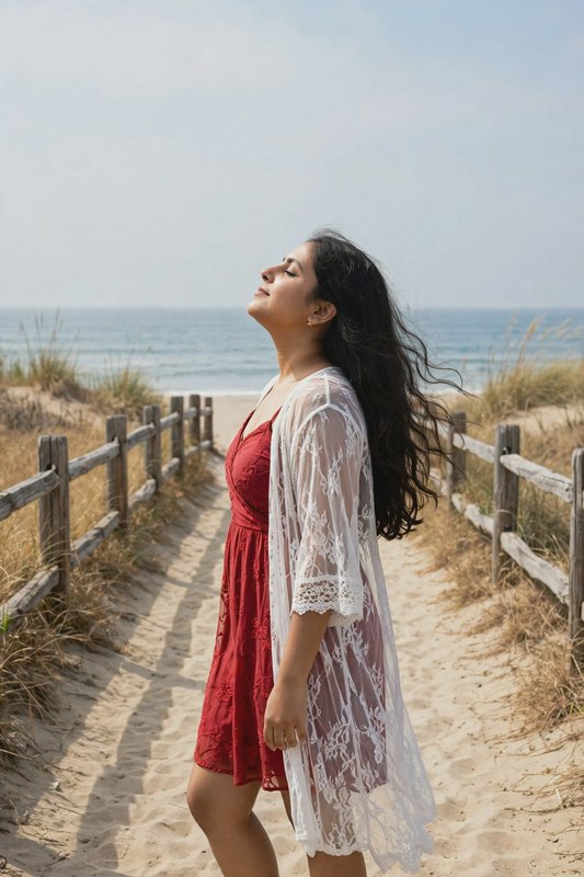 Woman with long dark hair tilts her face upward while standing on a sandy beach path