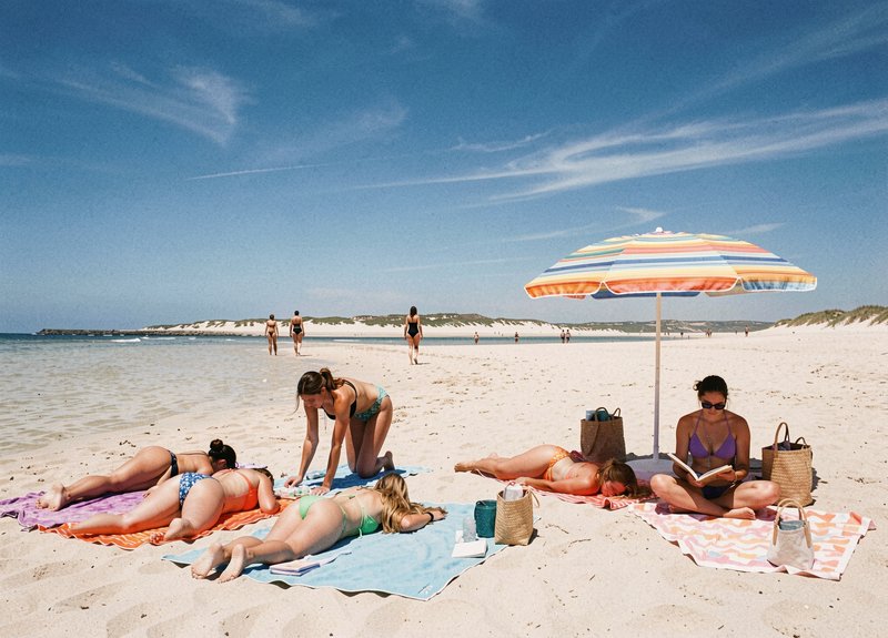 Group of women friends relax and sunbathe on a sunny sandy beach under a colorful striped beach u...