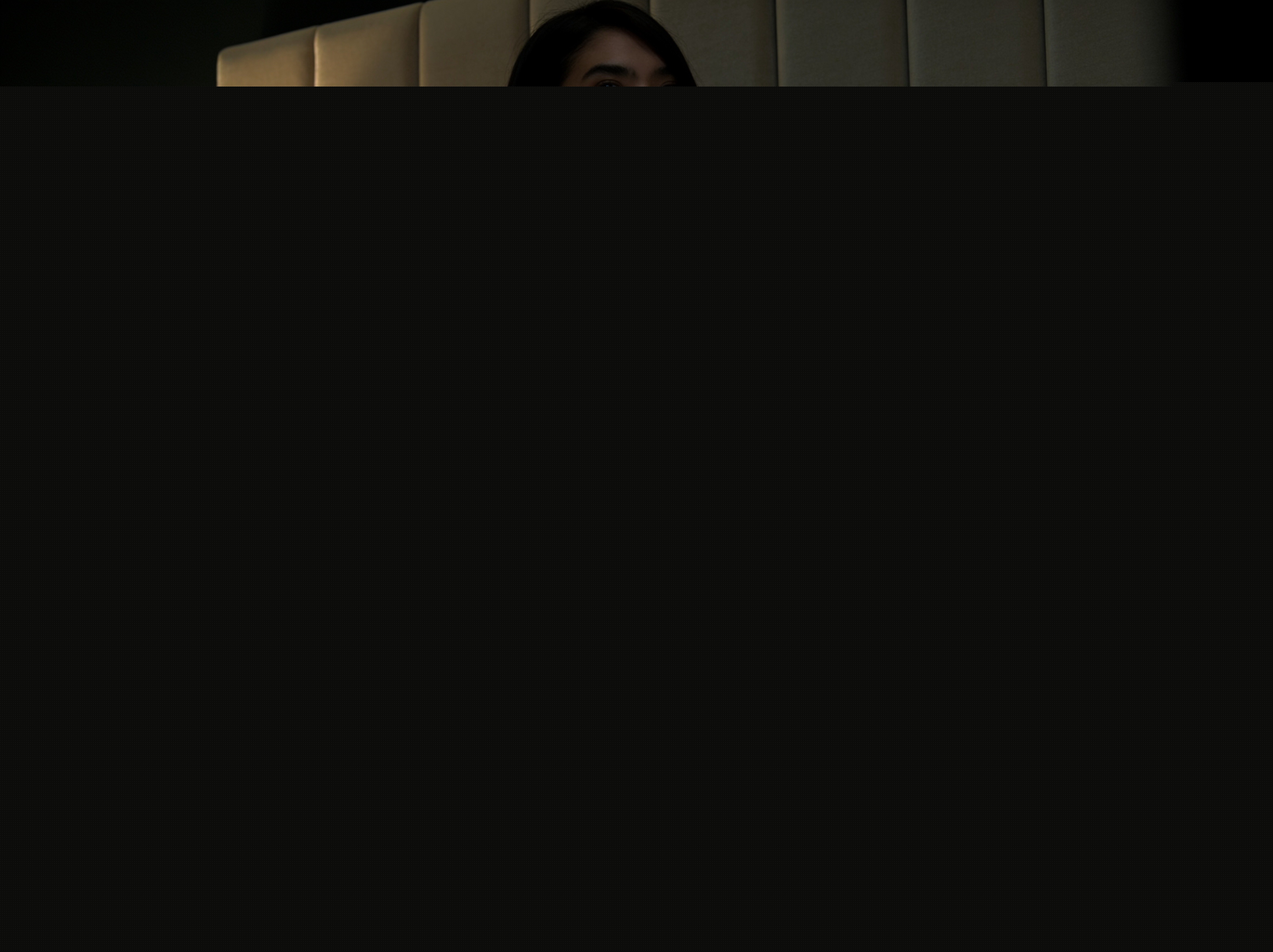 Partial shot of a person's eyes and dark hair peeking above a gray obscuring bar, against a tufte...