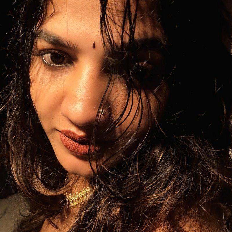 Close-up dramatic portrait of a South Asian woman with a bindi, nose pin, and wet wavy hair lit by warm low lighting