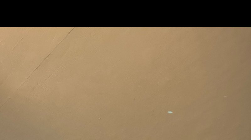 Close up of warm matte tan wall surface with thin diagonal scratch, small specks, and solid black...