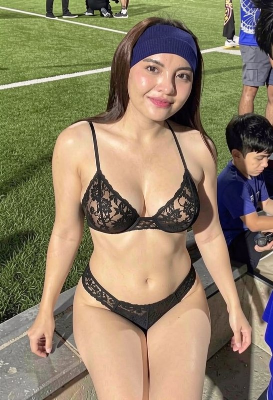 Woman in black lace lingerie and navy headband poses on a sports field sideline