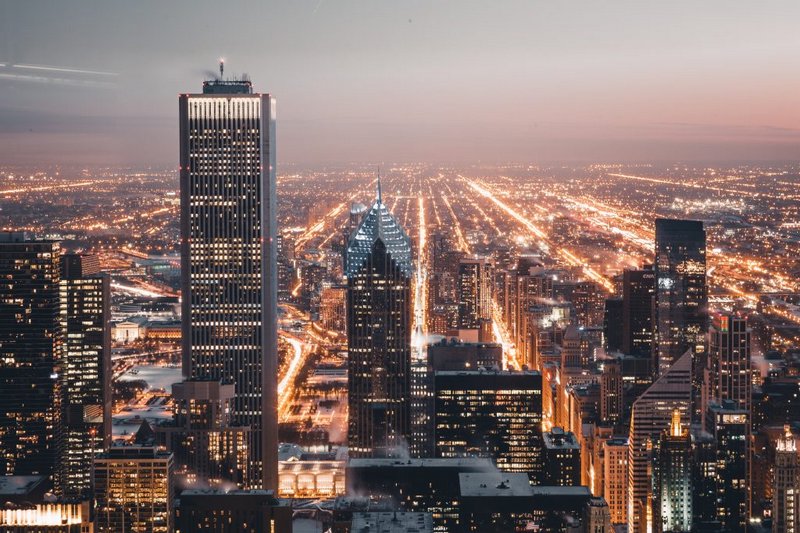 Aerial view of downtown Chicago skyline at dusk, with glowing street lights stretching across the...