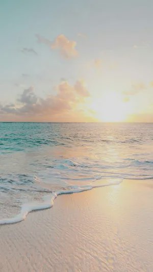 Sunset over a calm ocean with gentle waves washing onto a sandy beach.