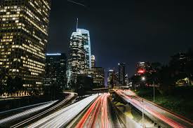 Night cityscape with illuminated skyscrapers and streaking car light trails on a highway.