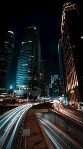 Night cityscape with tall skyscrapers and long-exposure light trails on a highway.