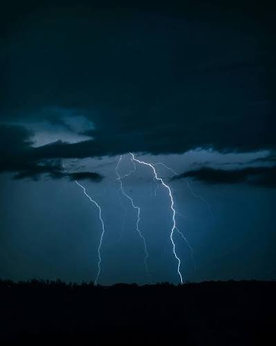 Dark night sky with bright jagged lightning bolts striking down over a silhouetted horizon.