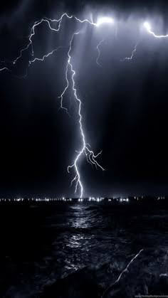 Lightning bolt striking over a dark sea with city lights on the horizon.
