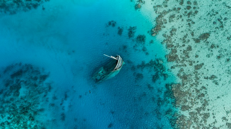 Aerial top-down view of a partially submerged shipwreck resting in clear turquoise tropical ocean...