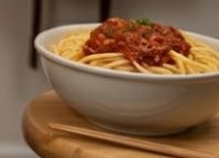Bowl of spaghetti with tomato meat sauce on a wooden board.