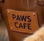 Sign reading "PAWS CAFE" on a wooden board with warm lighting.