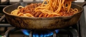 Skillet of spaghetti with meat sauce on a stove, being stirred with tongs