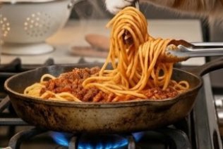 Spaghetti bolognese being twirled on a fork over a sizzling skillet.