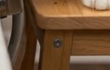 A close-up of a wooden chair leg and corner with a visible screw.