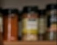 Row of glass spice jars with colorful labels on a wooden shelf.