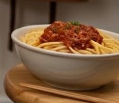 Bowl of spaghetti with meat sauce on a wooden table.