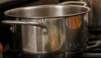 A shiny stainless steel pot with handles sits on a stove top.