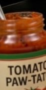 Close-up of a glass jar filled with orange-red tomato sauce, with part of the label visible.