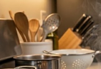 Kitchen counter with wooden spoons, a colander, pots, and a knife block in warm, softly lit light...