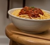 Bowl of spaghetti with meat sauce on a wooden stool.