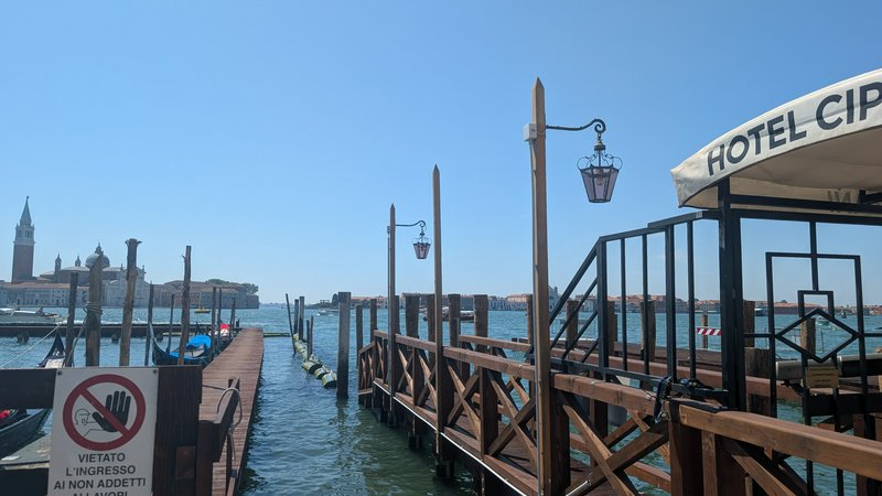 [Private Hotel Cipriani wooden dock on the Venice lagoon, view of San Giorgio Maggiore under a clear bright blue sky]