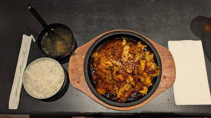 Overhead view of Korean spicy bulgogi meal set with stir fry, rice, soup, and chopsticks on a bla...