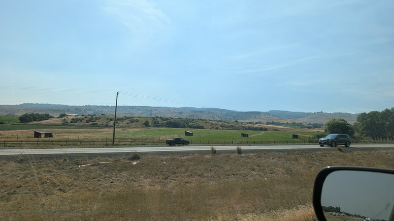 View from a moving car of a rural highway, rolling pastoral farmland, distant hills, and passing ...