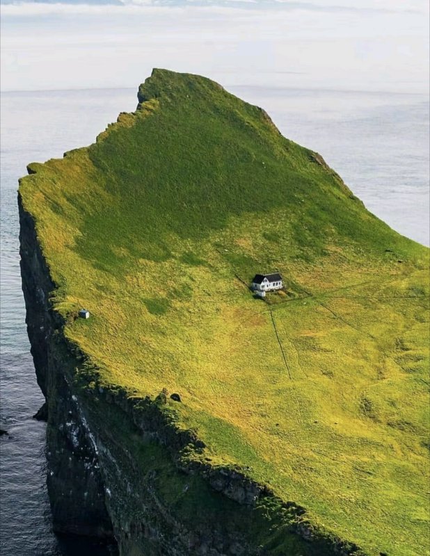 Isolated small white house perched on a grassy remote ocean sea stack island