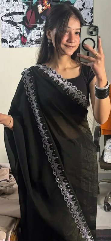 Young South Asian woman takes a mirror selfie wearing a black saree with shimmering silver embroi...