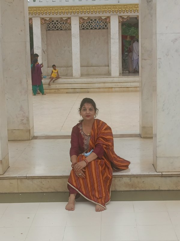 Woman in traditional Indian attire sits barefoot on marble temple steps, other visitors visible in the ornate temple
