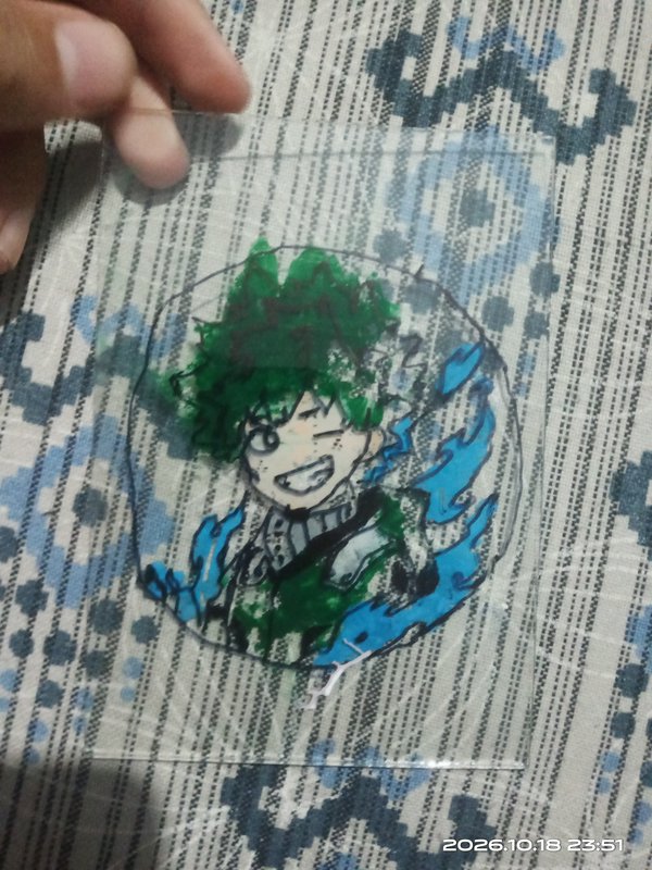 Hand holding a hand-painted clear acrylic charm of chibi Izuku Midoriya over patterned fabric