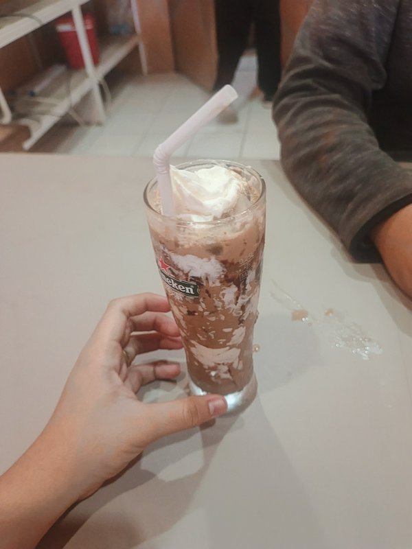 Hand holding tall iced chocolate drink topped with whipped cream on a light cafe table