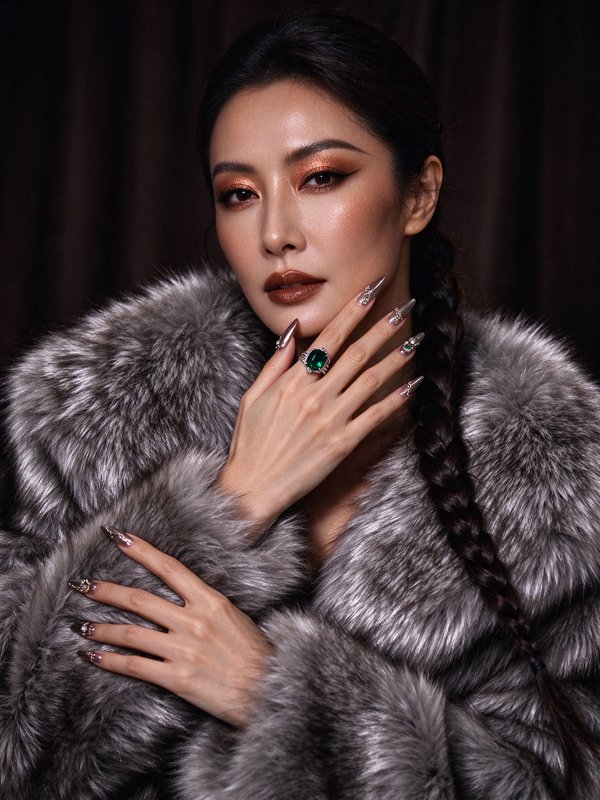 Elegant woman in plush grey fur coat displays her statement emerald ring and crystal stiletto man...